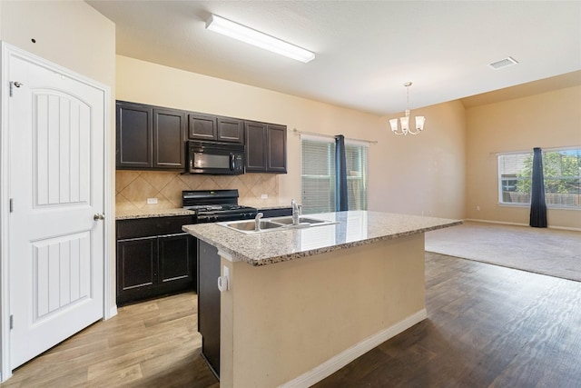 kitchen with decorative backsplash, an island with sink, sink, light hardwood / wood-style floors, and black appliances