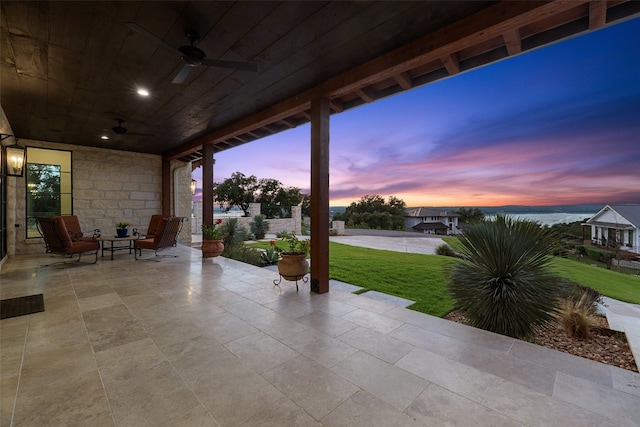 patio terrace at dusk featuring ceiling fan and a lawn