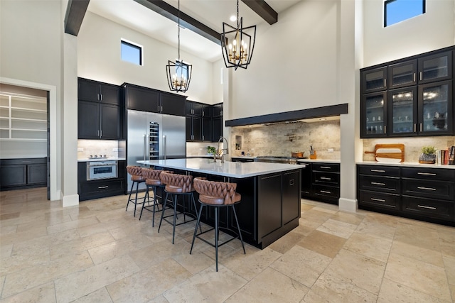 kitchen featuring beamed ceiling, a center island with sink, backsplash, and a high ceiling