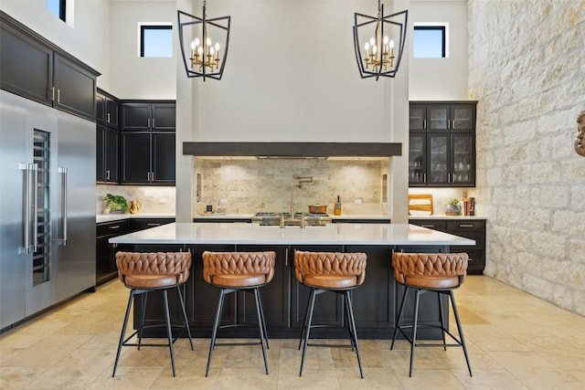 kitchen with a towering ceiling, a kitchen island with sink, stainless steel built in fridge, and a breakfast bar