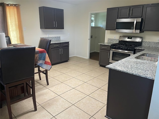 kitchen with stainless steel appliances, light tile patterned flooring, and light stone countertops