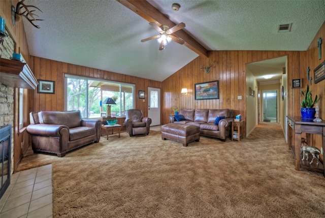 living room with a textured ceiling, wooden walls, ceiling fan, and a stone fireplace