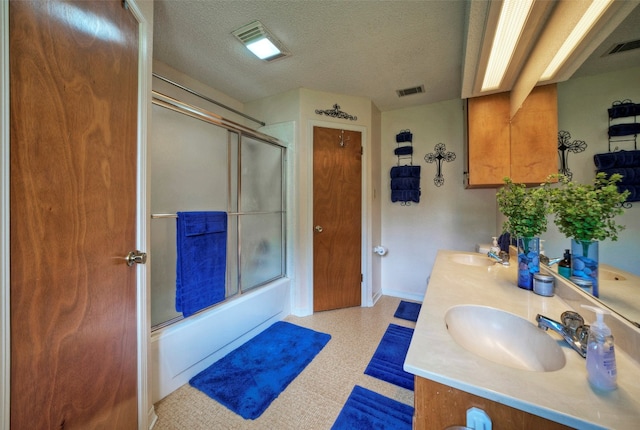 bathroom featuring vanity, bath / shower combo with glass door, and a textured ceiling