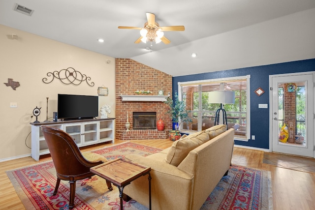 living room with lofted ceiling, light wood-type flooring, ceiling fan, a fireplace, and brick wall