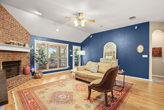 living room featuring ceiling fan, light wood-type flooring, lofted ceiling, and a brick fireplace