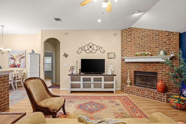 living room with lofted ceiling, a fireplace, light hardwood / wood-style flooring, and ceiling fan with notable chandelier