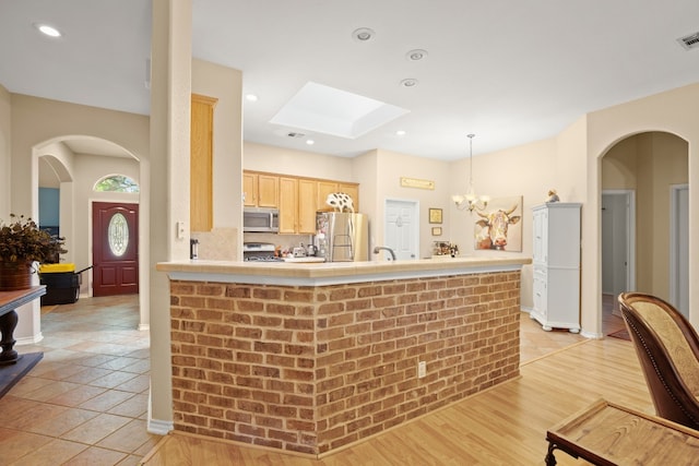 kitchen featuring light wood-type flooring, a notable chandelier, appliances with stainless steel finishes, light brown cabinetry, and decorative backsplash