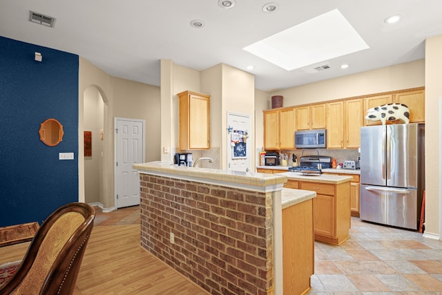 kitchen featuring light brown cabinets, stainless steel appliances, a skylight, light hardwood / wood-style flooring, and kitchen peninsula