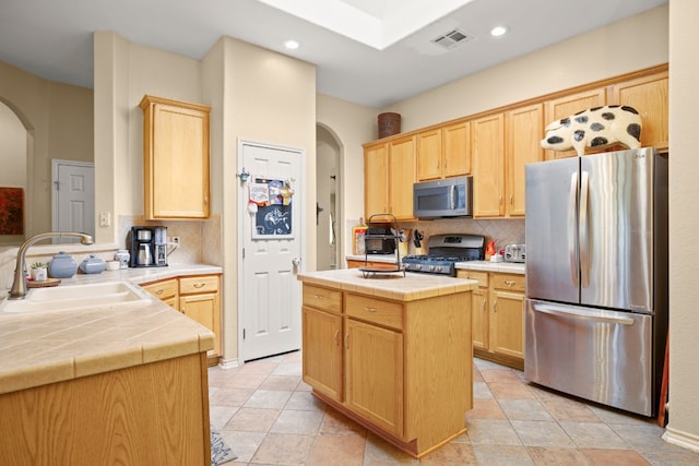 kitchen with stainless steel appliances, tile counters, a kitchen island, sink, and tasteful backsplash