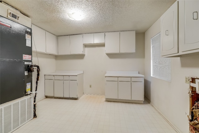 kitchen with a textured ceiling, heating unit, white cabinetry, and light tile patterned flooring