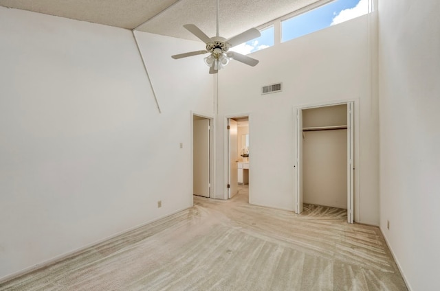 unfurnished bedroom featuring a textured ceiling, a closet, ceiling fan, a towering ceiling, and light carpet