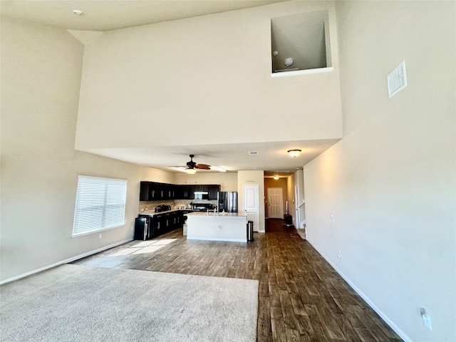 unfurnished living room featuring a towering ceiling, dark wood-type flooring, and ceiling fan