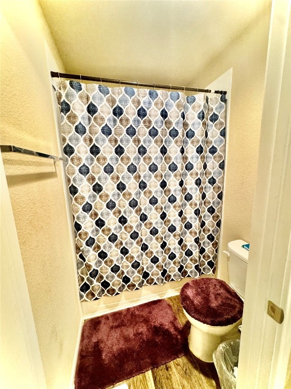 bathroom featuring toilet, walk in shower, and wood-type flooring