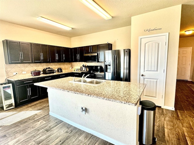 kitchen featuring tasteful backsplash, appliances with stainless steel finishes, sink, light wood-type flooring, and a kitchen island with sink