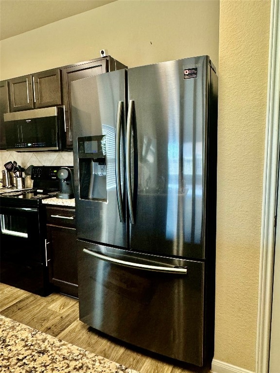 kitchen featuring decorative backsplash, light stone countertops, dark brown cabinetry, light wood-type flooring, and appliances with stainless steel finishes