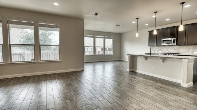 kitchen with a breakfast bar, light stone counters, decorative light fixtures, dark brown cabinets, and plenty of natural light