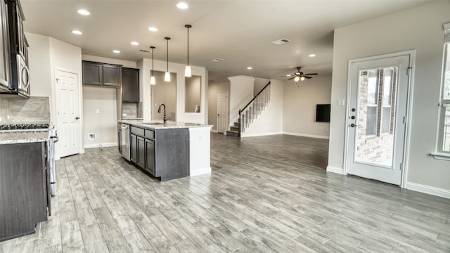 kitchen featuring sink, hanging light fixtures, dark brown cabinets, light stone countertops, and an island with sink