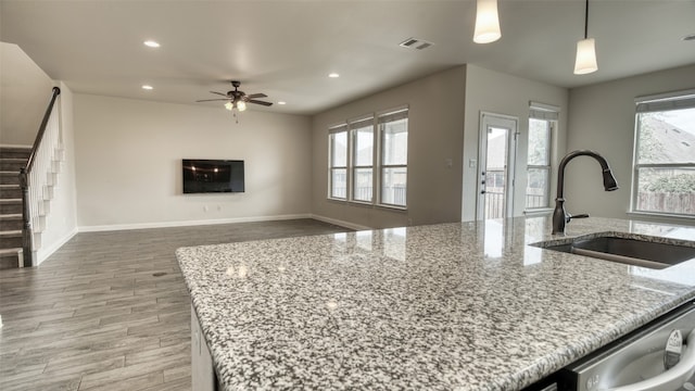 kitchen with wood-type flooring, sink, hanging light fixtures, ceiling fan, and light stone countertops