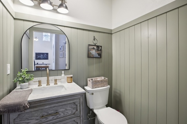 bathroom with wood walls, vanity, and toilet