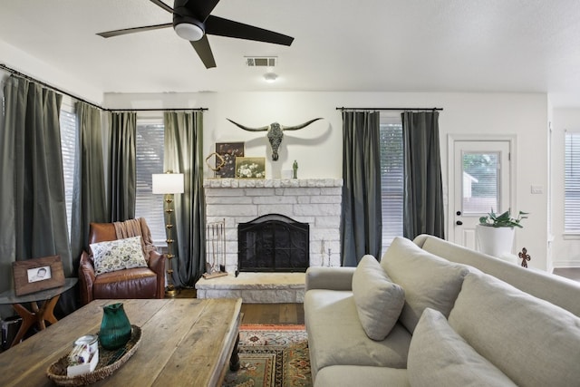 living room with a stone fireplace, ceiling fan, and wood-type flooring