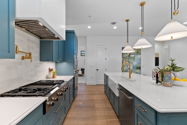 kitchen with backsplash, appliances with stainless steel finishes, decorative light fixtures, sink, and light wood-type flooring