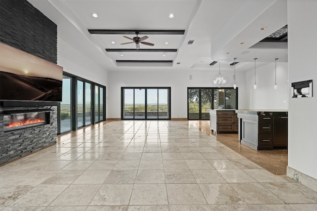 unfurnished living room with a towering ceiling, a fireplace, a raised ceiling, and ceiling fan with notable chandelier