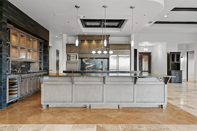 kitchen with a spacious island, built in appliances, a raised ceiling, pendant lighting, and beverage cooler