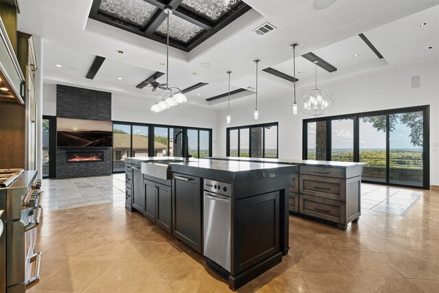 kitchen with a stone fireplace, sink, hanging light fixtures, a kitchen island with sink, and high end stainless steel range