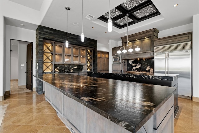 kitchen with a spacious island, decorative light fixtures, built in appliances, dark brown cabinets, and decorative backsplash