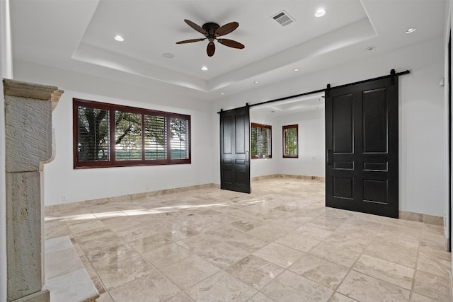 unfurnished bedroom with ceiling fan, a tray ceiling, and a barn door