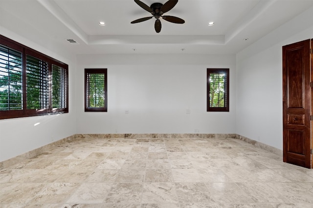 empty room featuring a wealth of natural light, a raised ceiling, and ceiling fan