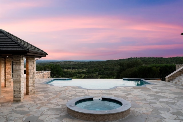 pool at dusk featuring an in ground hot tub and a patio area