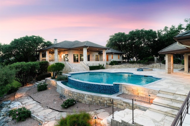 pool at dusk featuring a patio and an in ground hot tub