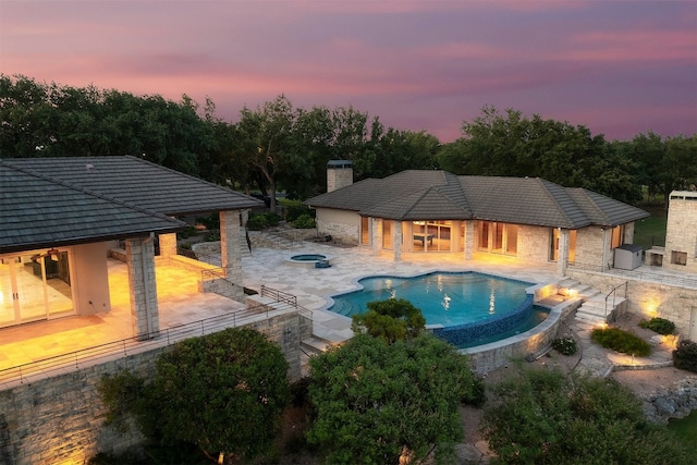 pool at dusk featuring a patio and an in ground hot tub