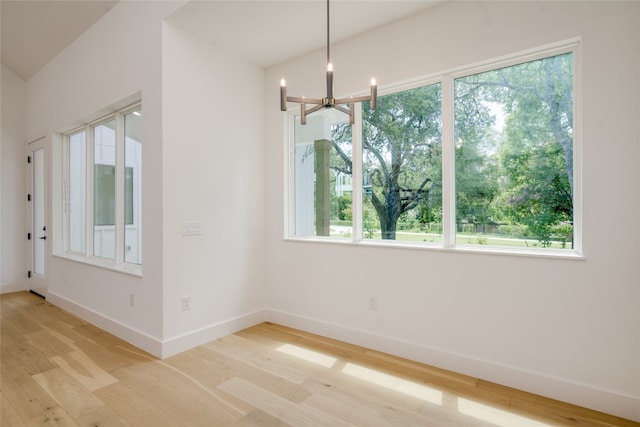 unfurnished dining area with light wood-type flooring, a healthy amount of sunlight, and a chandelier