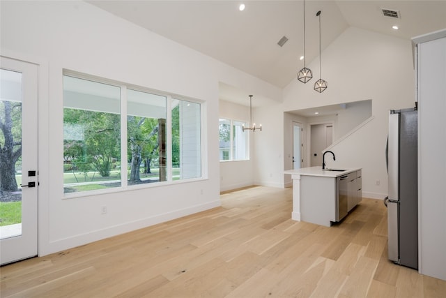 kitchen with light wood-type flooring, a notable chandelier, sink, decorative light fixtures, and stainless steel appliances