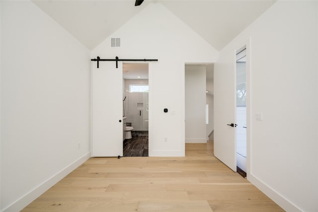 unfurnished bedroom featuring light wood-type flooring, high vaulted ceiling, a barn door, ceiling fan, and connected bathroom