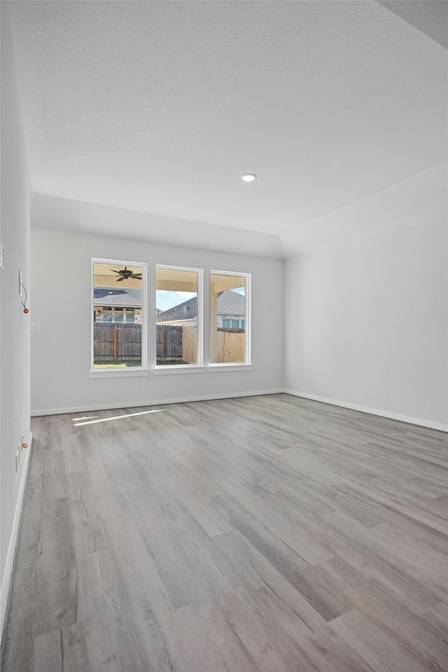 spare room featuring ceiling fan, lofted ceiling, and light wood-type flooring