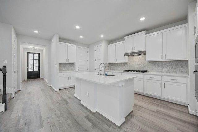 kitchen with sink, light hardwood / wood-style floors, white cabinets, and a center island with sink