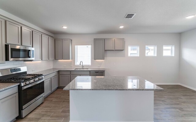 kitchen with light wood-type flooring, sink, light stone countertops, appliances with stainless steel finishes, and a center island