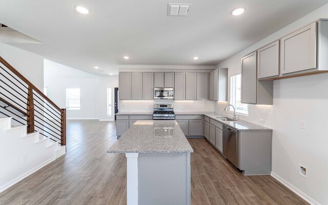 kitchen with light stone countertops, sink, light hardwood / wood-style floors, appliances with stainless steel finishes, and gray cabinets