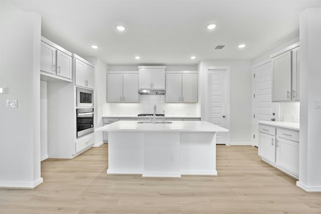 kitchen featuring light hardwood / wood-style flooring, a kitchen island with sink, tasteful backsplash, white cabinets, and oven