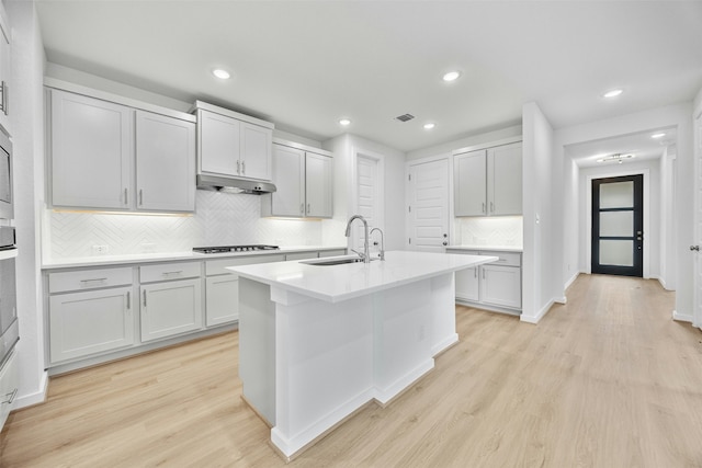 kitchen with sink, backsplash, gas stovetop, a center island with sink, and light wood-type flooring