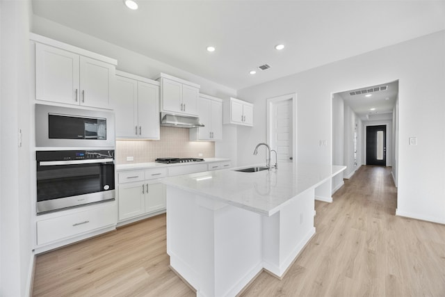 kitchen with white cabinetry, sink, oven, gas cooktop, and a center island with sink