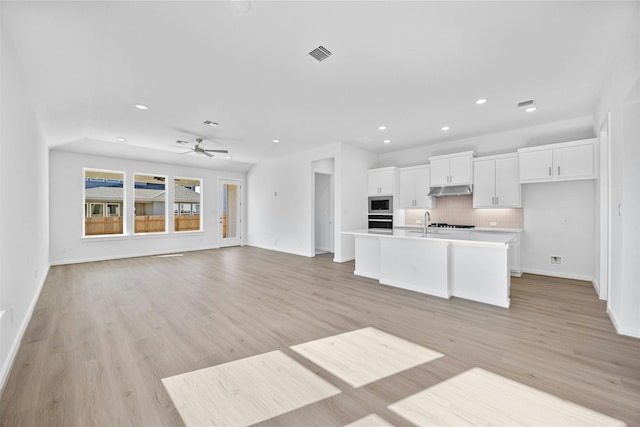 kitchen with light hardwood / wood-style flooring, appliances with stainless steel finishes, white cabinets, a center island with sink, and decorative backsplash