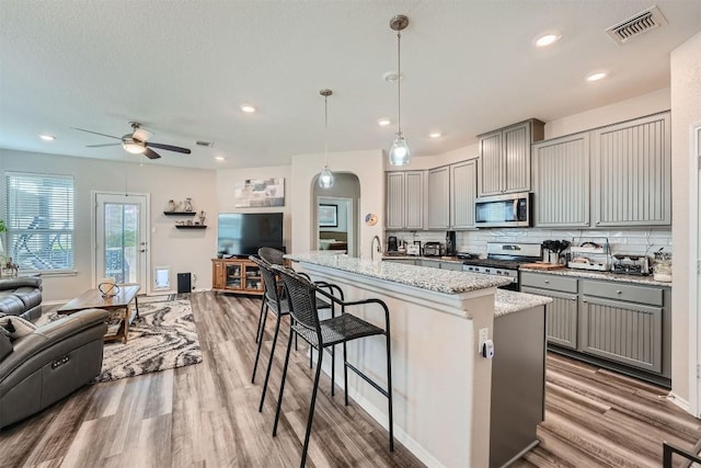 kitchen with tasteful backsplash, gray cabinetry, stainless steel appliances, pendant lighting, and an island with sink