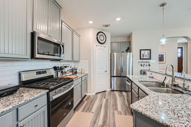 kitchen with backsplash, hanging light fixtures, sink, gray cabinets, and appliances with stainless steel finishes