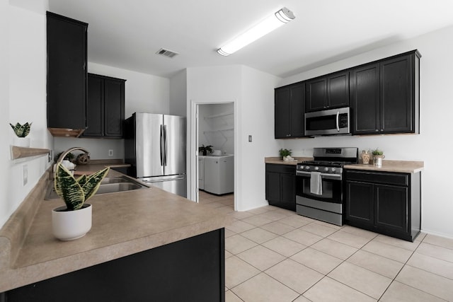 kitchen featuring sink, light tile patterned floors, stainless steel appliances, and washer and dryer