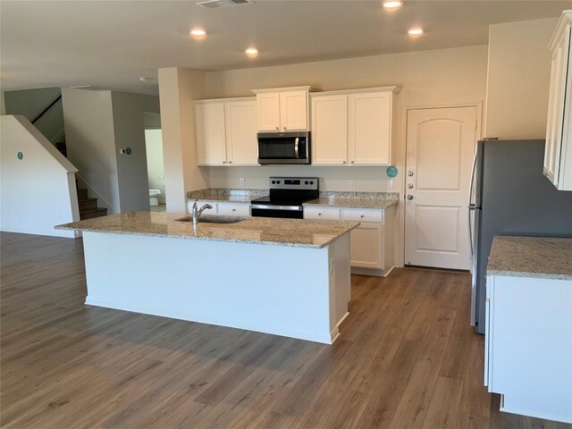 kitchen featuring appliances with stainless steel finishes, an island with sink, sink, white cabinets, and light stone countertops