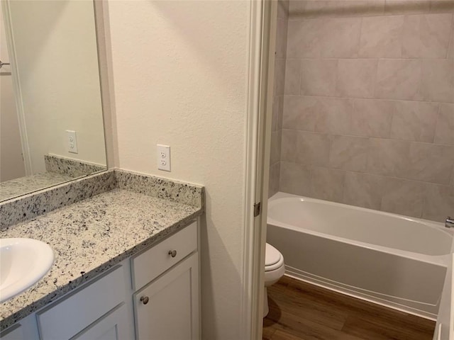 full bathroom with vanity, tiled shower / bath, hardwood / wood-style floors, and toilet